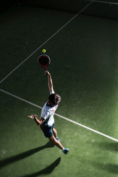 Male athlete servicing ball while playing padel tennis in sports court at night
