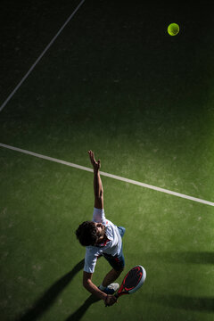 Male athlete servicing ball while playing padel tennis in sports court at night