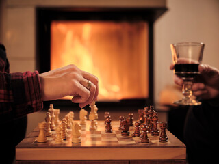 Mature man with wine glass while woman playing chess by fireplace in living room