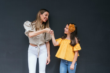 Cheerful mother and daughter giving fist bump while standing against black background