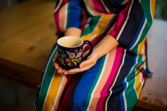 Woman in multi colored clothing holding coffee cup while sitting on table at home