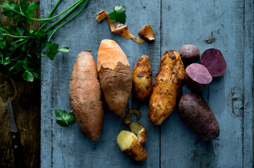 Parsley and different varieties of potatoes lying on wooden surface