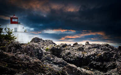 A traditional lighthouse on the rocky West Coast of Vancouver Island near Pacific Rim National Park under a dramatic sky.