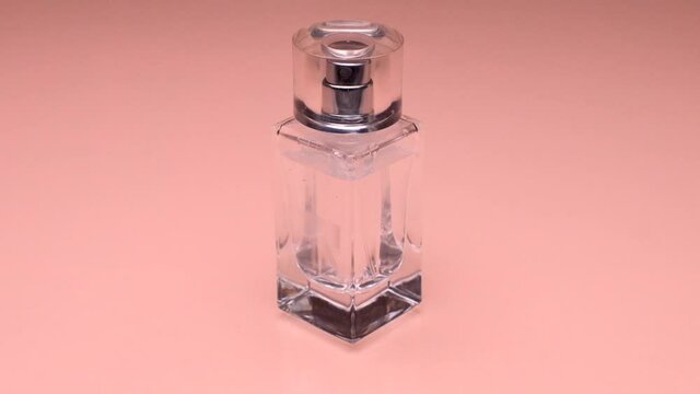 Close-up. A White Ribbon Wraps Around A Bottle Of Transparent Perfume And Flies Away. Scent. A Pink Background