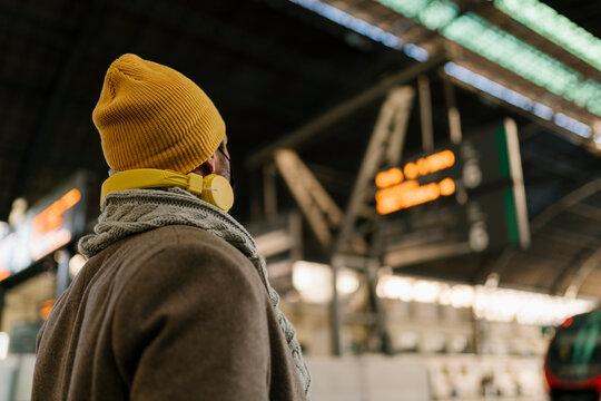 Man wearing knit hat checking arrival departure board while standing at station