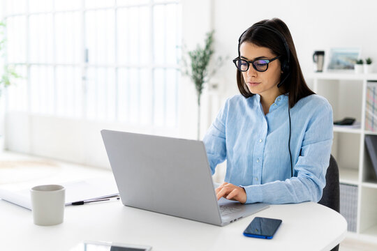 Female customer service representative with headset working on laptop while sitting at office