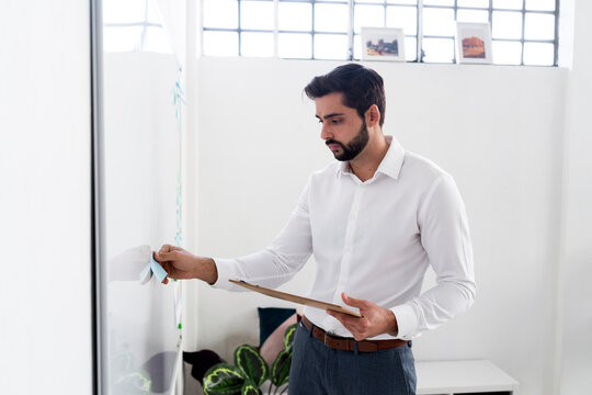 Young businessman with clipboard sticking adhesive note on whiteboard at work place