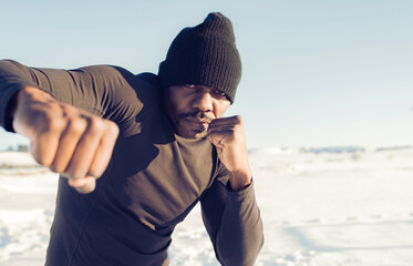 Male athlete wearing knit hat showing fist while practicing boxing outdoors