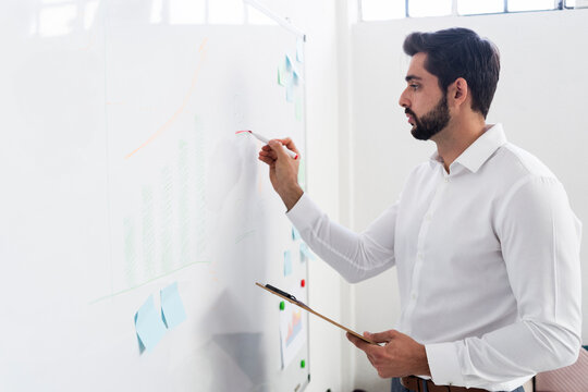 Male Entrepreneur Drawing Business Graph On Whiteboard At Work Place