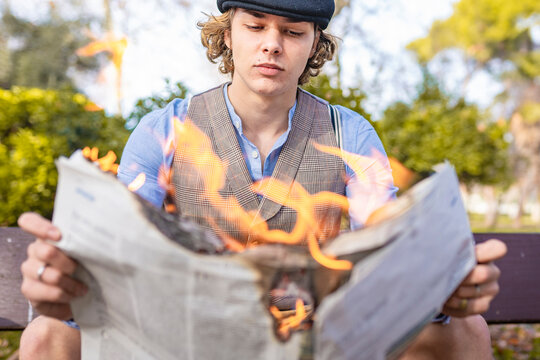 Young man reading lit newspaper while sitting in park