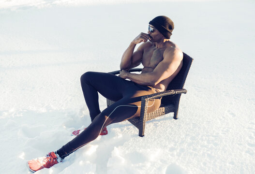Thoughtful shirtless sportsman looking away while sitting on chair in snow
