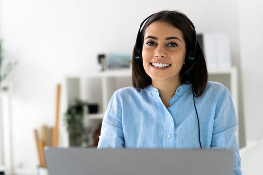 Customer service representative wearing headset smiling while using laptop at office
