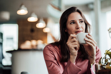 Businesswoman holding coffee cup while contemplating in cafe