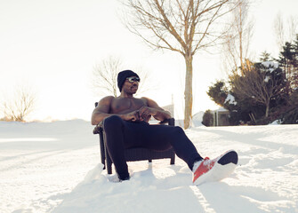 Shirtless sportsman relaxing while sitting on chair during winter