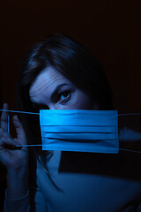 the photo of a woman holding mask in her hands with surprised face expression  in a blue light over the dark background