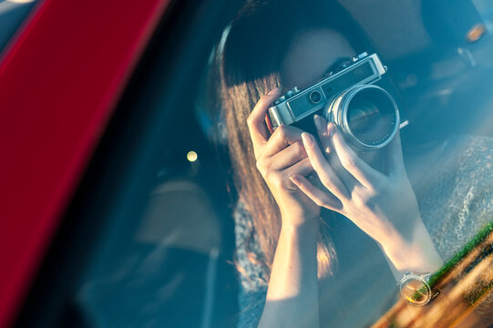 Fototapeta Young woman photographing from vintage camera through car glass window