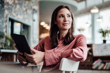 Female professional with digital tablet looking away while sitting cafe