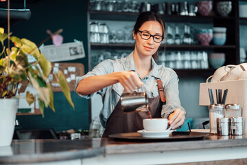Female owner pouring coffee in cup at cafe