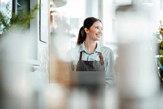 Smiling female entrepreneur with laptop looking away at cafe