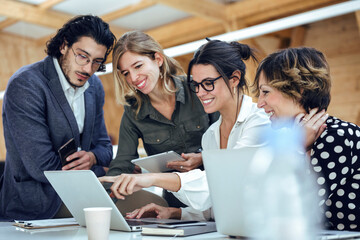 Smiling professionals discussing over laptop at office