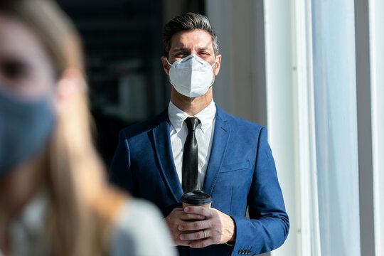 Businessman wearing protective face mask holding coffee while standing in office