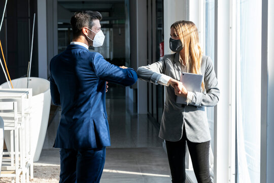 Businessman giving elbow bump to colleague while standing in office during COVID-19