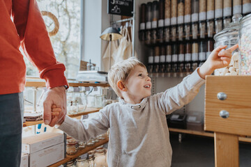 Cheerful boy holding hand of father while pointing at candy jar in store