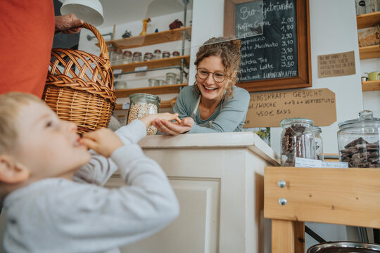 Smiling female entrepreneur giving treat to little boy in zero waste store