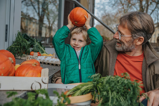 Smiling father looking at playful son holding pumpkin while shopping at shop