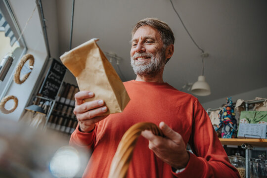 Happy mature man looking at brown package while standing in retail store