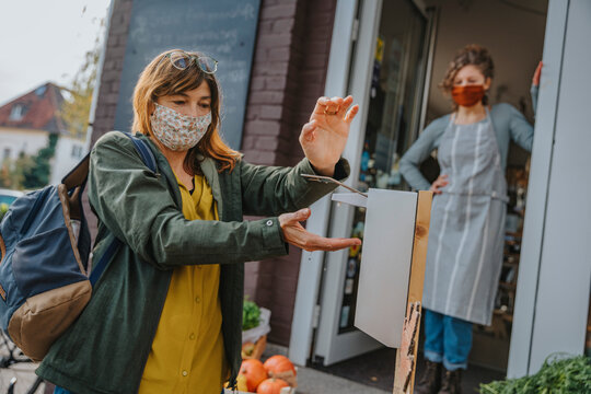 Mature female customer disinfecting hands with sanitizer before entering organic store