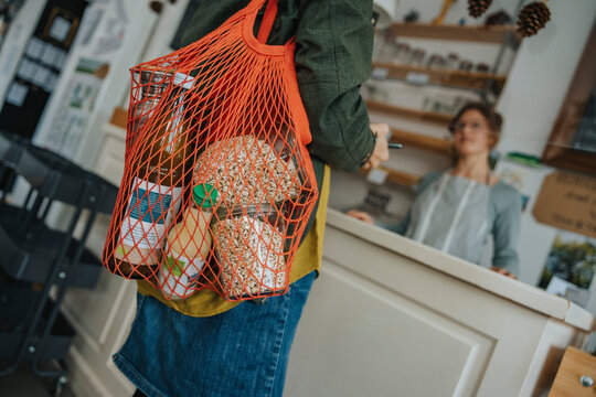 Female customer carrying mesh bag full of groceries in retail store