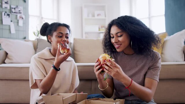 Portrait of young sisters indoors at home, eating burgers.
