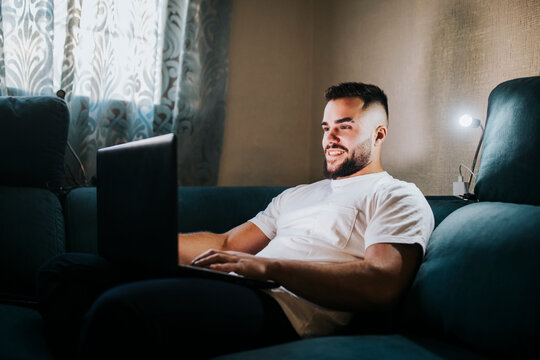 Smiling male entrepreneur working on laptop while sitting on couch in living room