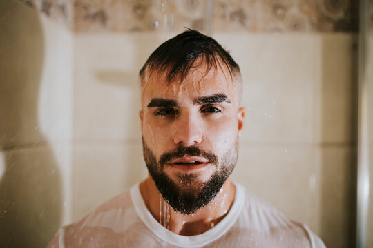 Bearded wet man with t-shirt taking shower in bathroom at home