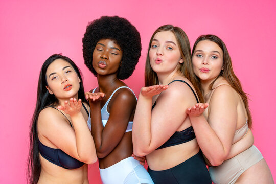 Multi-ethnic group of female models in lingerie blowing kisses against pink background