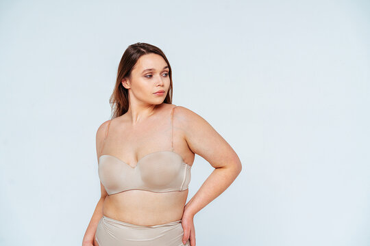 Confident woman in lingerie looking away while standing with hand on hip in studio