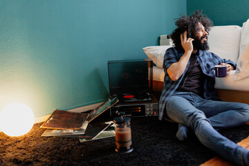 Hipster man with coffee cup listening music through turntable while sitting in living room