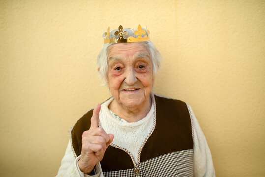 Close-up of smiling senior woman wearing paper crown gesturing against wall