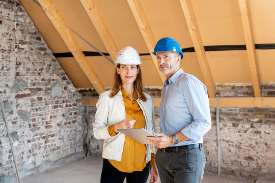 Architect with digital tablet looking away while standing by businesswoman at construction site