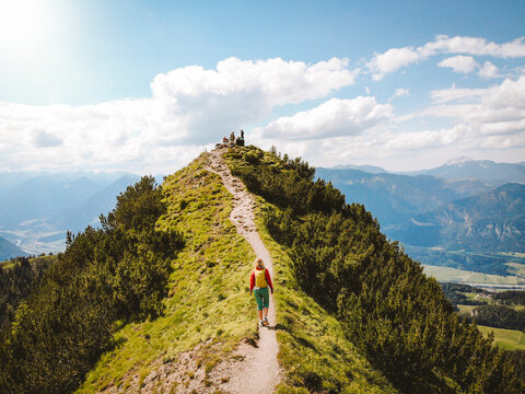 Drone shot of woman hiking on mountain towards peak against sky