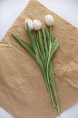 bouquet of white tulips lies on kraft paper on white paper background