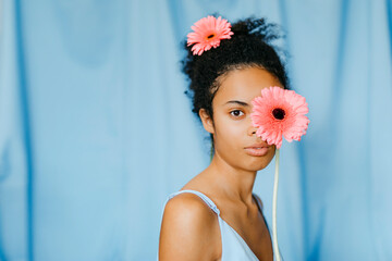 Young woman with gerbera daisy in front of eye against blue curtain