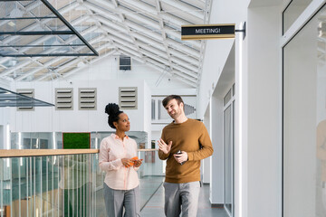 Creative businessman discussing with female colleague while walking in corridor at office