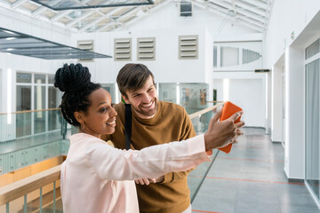 Smiling multi-ethnic male and female colleagues taking selfie through smart phone at workplace
