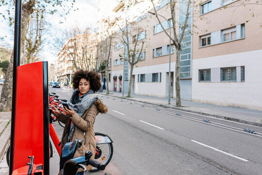 Young woman looking away while standing by ticket machine at bicycle parking station in city