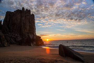 Golden sunrise on the Sea of Cortez by giant rock formations on the sandy beach.