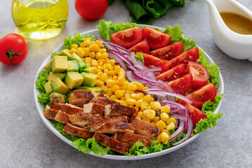 Rainbow salad. Colorful mix green salad bowl with grilled chicken, avocado, tomato, lettuce, corn and red onion served in white plate with mustard dressing.