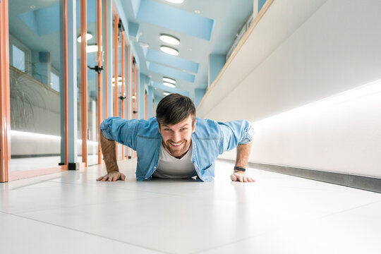 Smiling businessman doing push ups in office corridor