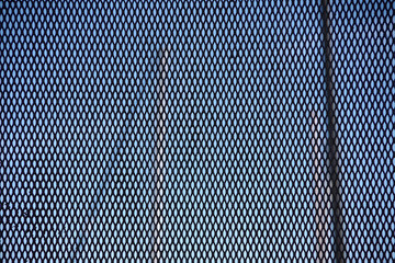Full frame close-up view of a section of the metal security fence at an ocean marina with sailboat masts and blue sky detectable in the background